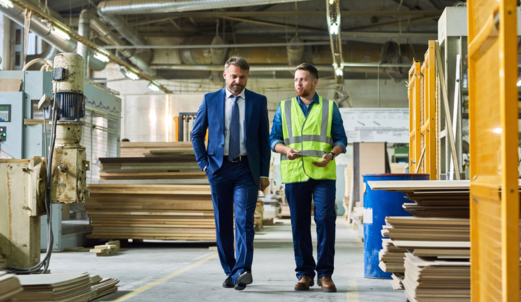 Full length portrait of young workman giving tour of modern factory to handsome mature businessman discussing possible investment, copy space