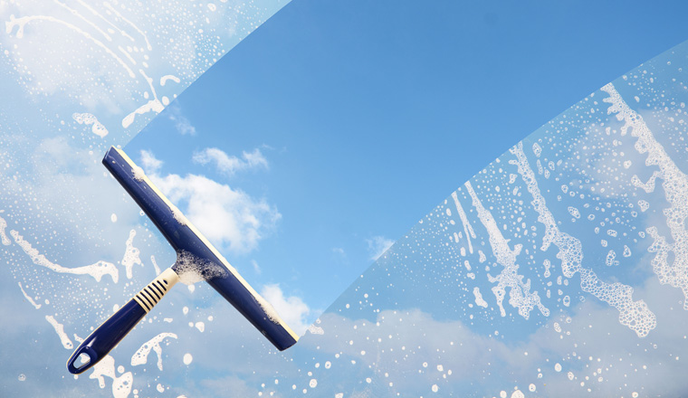 Rubber squeegee cleans a soaped window and clears a stripe of blue sky with clouds, concept for tranparency or spring cleaning, copy space in the background