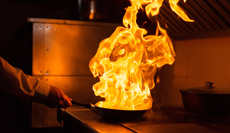 Flambe lamb rib roast. Cooking with fire in frying pan. Professional chef in a commercial kitchen cooking. Man frying food in flaming pan on hob in outdoor kitchen. slow motion .