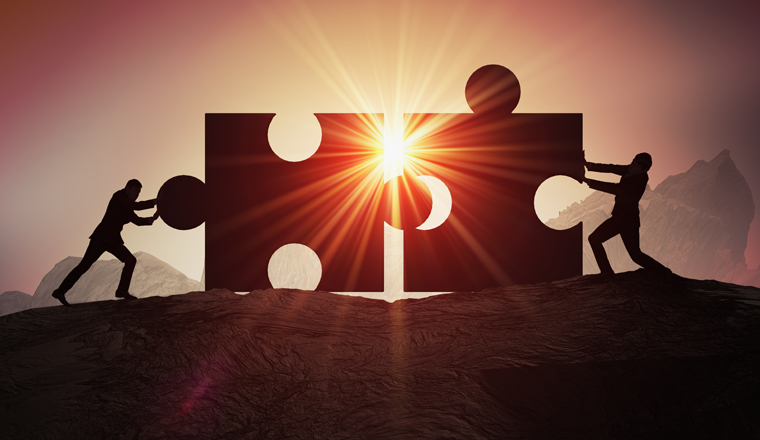 Teamwork, partnership and cooperation concept. Silhouettes of two businessman joining two pieces of puzzle together.