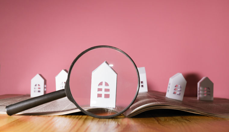 Magnifying glass in front of an open newspaper with paper houses. Concept of rent, search, purchase real estate.