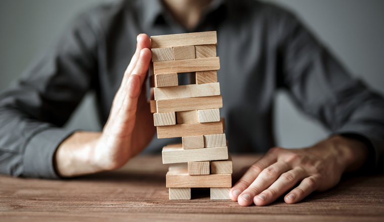 Businessman holds the model of business, made from wood blocks. Alternative risk concept, business plan and business strategy. Insurance concept.