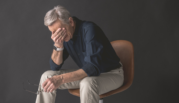 Tired old man closing face by hand while locating on seat. Fatigue during job concept