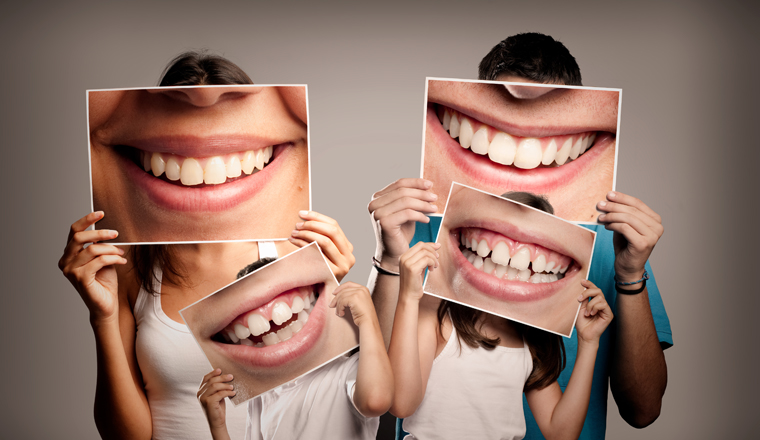 young family with children holding a picture of a mouth smiling on a gray background