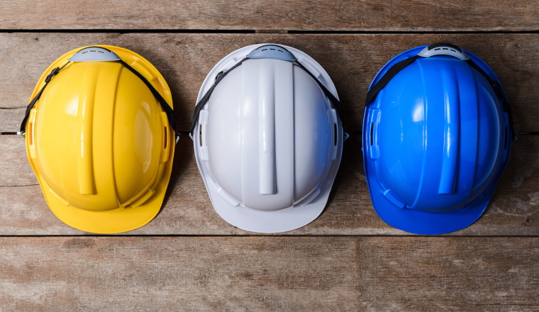 Yellow, White and Blue protective safety helmet on old wooden background. safety first concepts