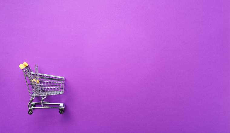 Shopping cart on violet background. Minimalism style. Creative design. Top view with copy space. Shop trolley at supermarket. Sale, discount, shopaholism concept. Consumer society trend.