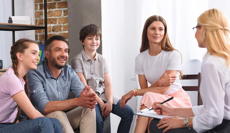 happy family sitting on therapy session by female counselor writing in clipboard in office 