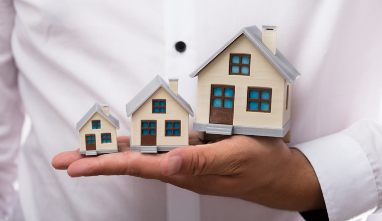 Close-up of a businessman's hand holding increasing size of house models