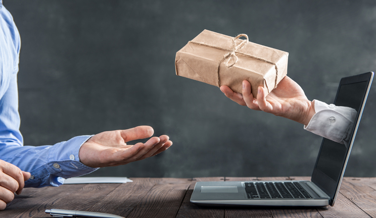 Hand coming out of the laptop gives the package to the businessman at the desk. The concept of ordering things via internet