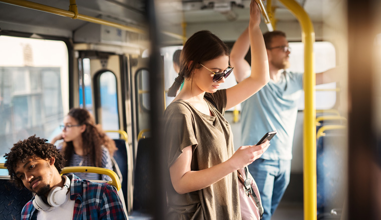 Sweet girl with sunglasses in using phone while standing in a bus.