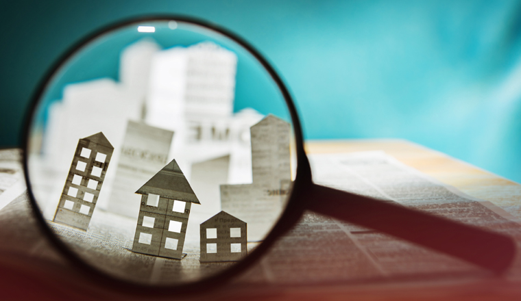 Magnifying glass in front of an open newspaper with paper houses. Concept of rent, search, purchase real estate.