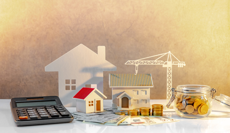 Real estate or property development. Construction business investment concept. Home mortgage loan rate. Coin stack on international banknotes with calculator, house and crane models on the table.