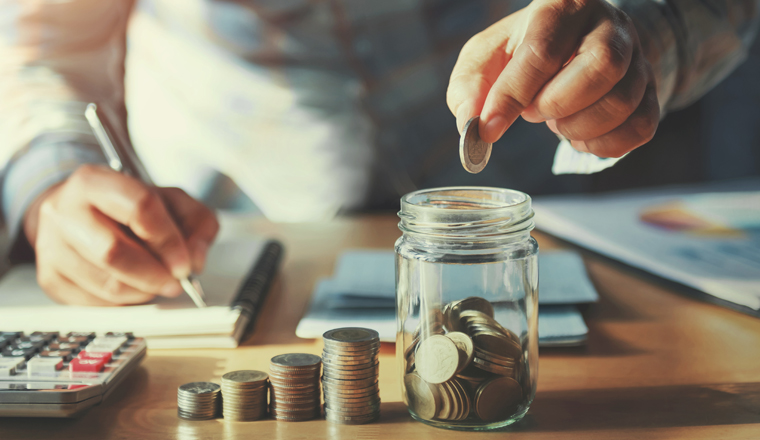 businessman saving money concept. hand holding coins putting in jug glass