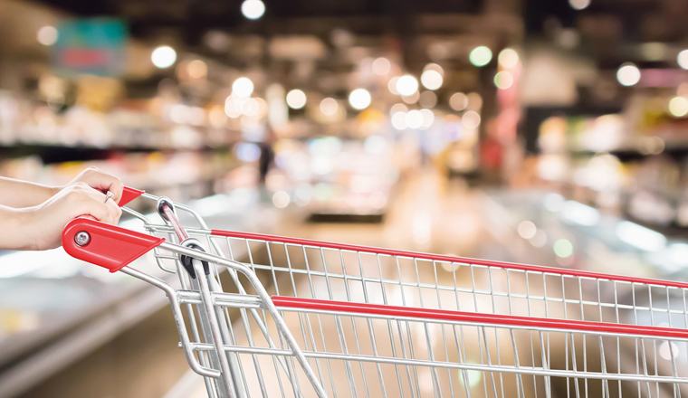 Woman hand hold empty red shopping cart with abstract blur supermarket discount store aisle interior defocused background with bokeh light