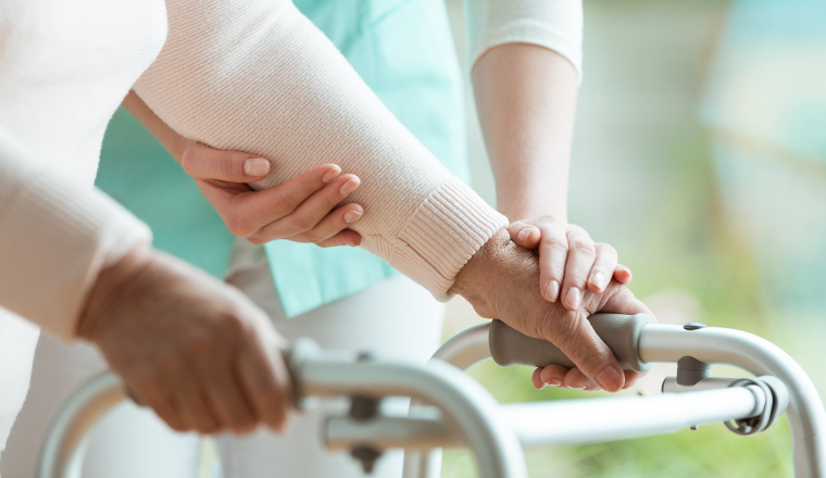 Closeup of senior lady's hands holding a walker and helpful nurse supporting her