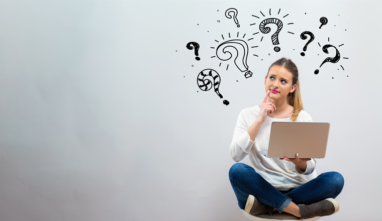 Question marks with young woman using her laptop on a grey background