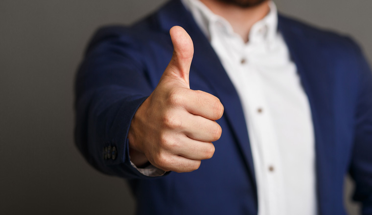 Excellent! Close-up of man in formalwear showing his thumb up while standing against blackboard