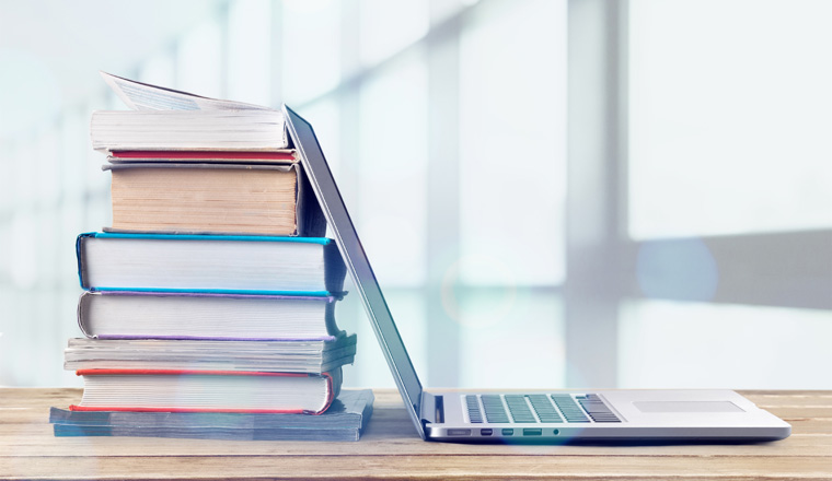 Stack of books with laptop on wooden table