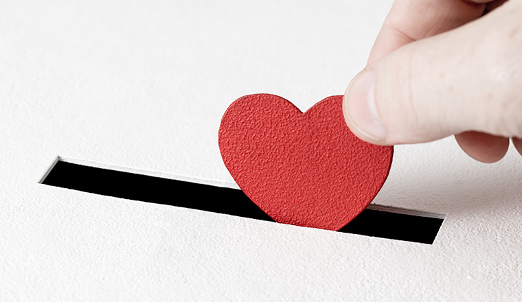 Hand of man inserts heart symbol into hole in donation box on white background with copy space. Concept of donor, life-saving or kindness