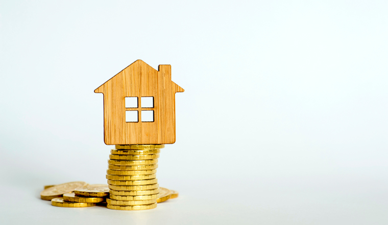 The house symbol is made of bamboo on a stack of yellow shiny coins on a light background. Real estate purchase offer concept. Copy space.