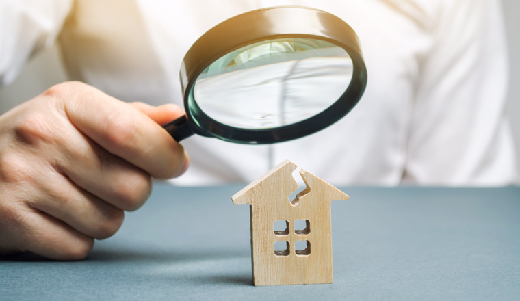 A man with a magnifying glass looks at a house with a crack. Damage assessment home and insurance risks. Estimation of the cost of repair and renovation of old buildings, property value.