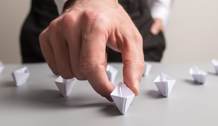 Wide view image of business executive holding the leading paper made boat of a group of many in a conceptual image of business leadership.