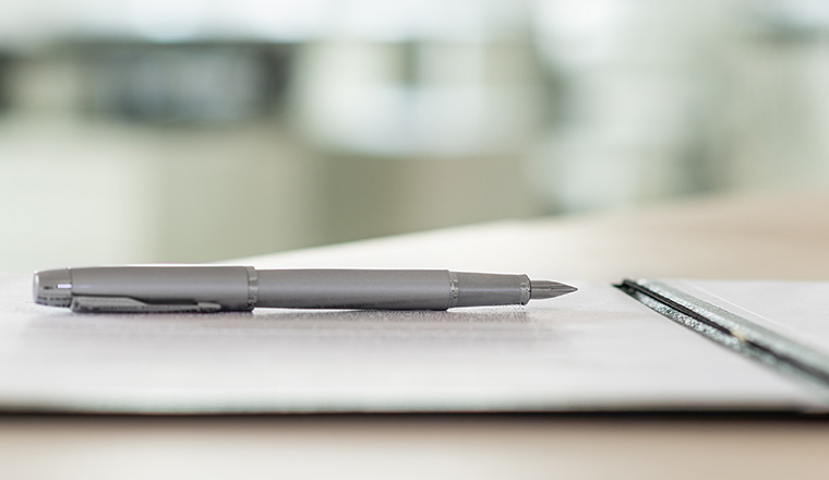 Wide view image of an ink pen lying on a contract in an open folder.