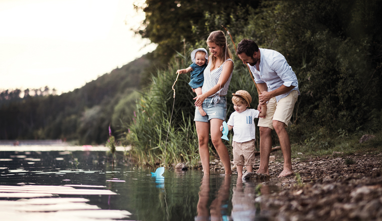 A young family with two toddler children spending time outdoors by the river in summer.