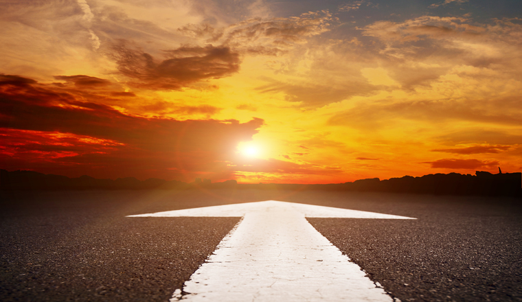 An empty asphalt road with the white arrow at sunset