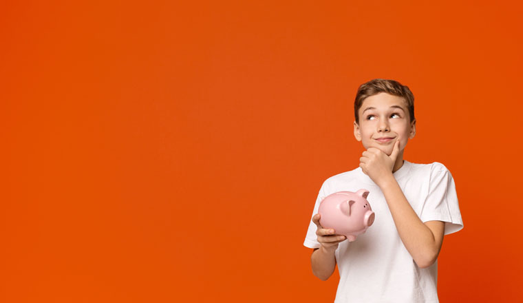 Teen boy with piggy bank dreaming about some things he can buy, orange studio background with empty space