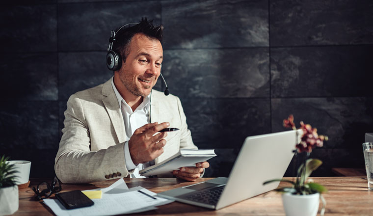 Businessman wearing linen suit sitting at his desk by the window and having online meeting in his office