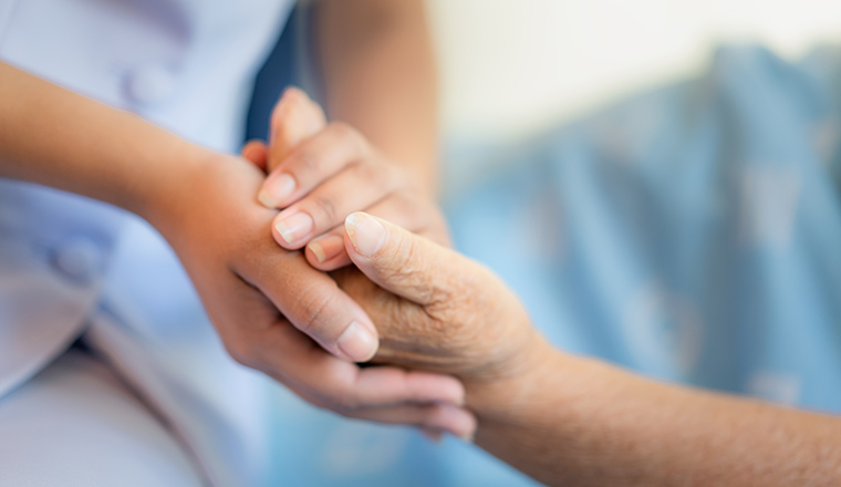 Nurse sitting on a hospital bed next to an older woman helping hands, care for the elderly concept