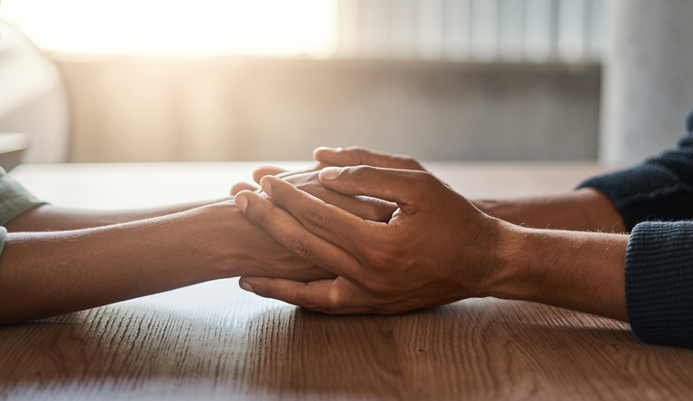 Close-up of couple holding each other's hand over the wooden desk in sunlight