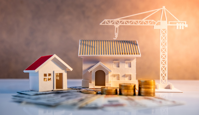 Real estate or property development. Construction business investment concept. Home mortgage loan rate. Coin stack on international banknotes with house and construction crane models on the table.