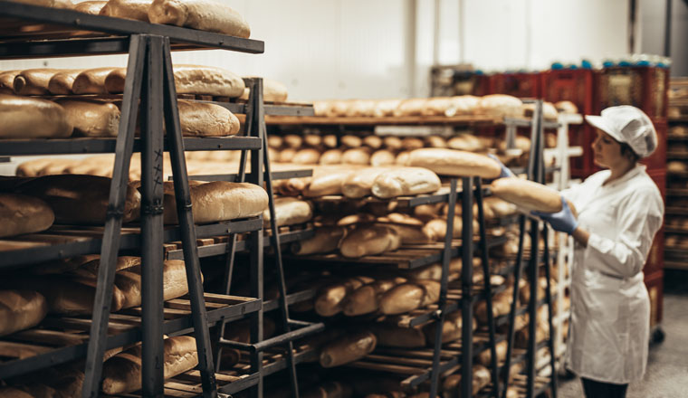 Young female worker working in bakery. She puts bread on shelf.