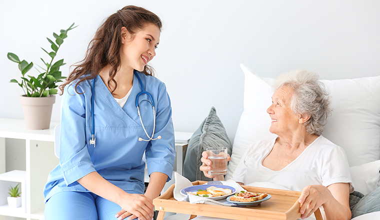 Young caregiver bringing senior woman breakfast in bed