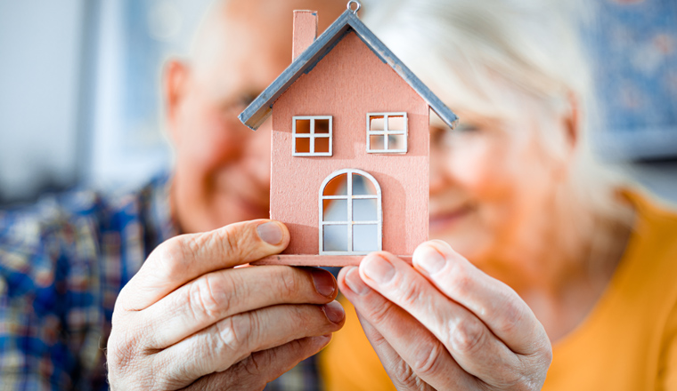 New house concept, happy senior couple holding small home model