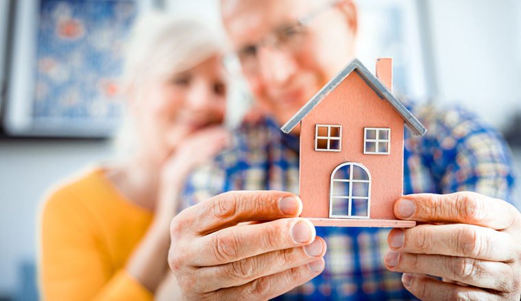 New house concept, happy senior couple holding small home model