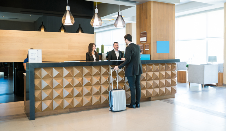 Businessman making booking at front desk with Latin receptionists in hotel lobby 