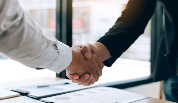 Entrepreneurs collaboration deal shaking hands in a modern office and financial paper graph on desk.