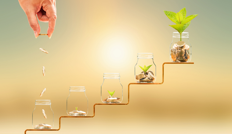 Investor hand hold and drop a gold coin in the five bottle and plant growing on golden steps on sunlight background, Business investment and saving money concept.