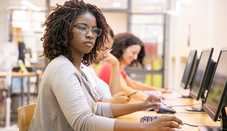 African American adult student working in computer class. Line of man and women in casual sitting at table, using desktops, typing. Staff training concept