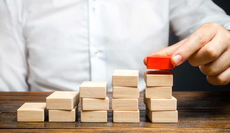 A man is building a ladder or growth chart from blocks. Strategy planning business expansion. Climbing the career ladder. Increase in income, organization of processors. Prioritization. Leadership