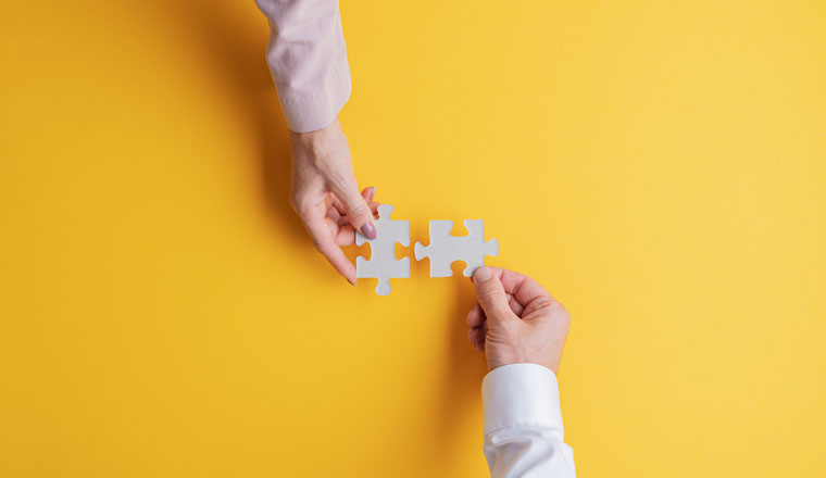 Top view of male and female hands joining two matching puzzle pieces together in a conceptual image. Over yellow background.