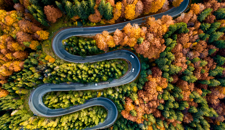 Perfect aerial view of winding forest road in the mountains. Colourful landscape with rural road, trees with yellow leaves. 