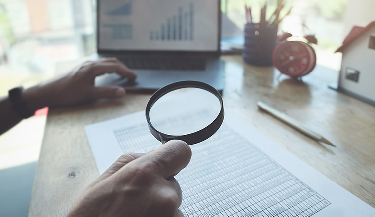 Business man using magnifying to review balance sheet annual with using  laptop computer to calculating budget. audit and Check integrity before investment concept.