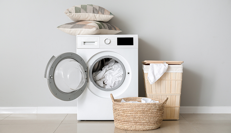 Modern washing machine with laundry near white wall