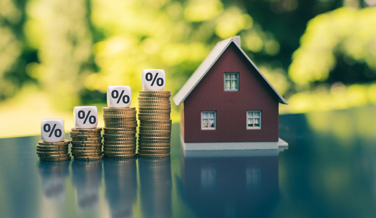 Symbol for increasing interest rates. Dice with percentage symbols on increasing high stacks of coins next to a model house.