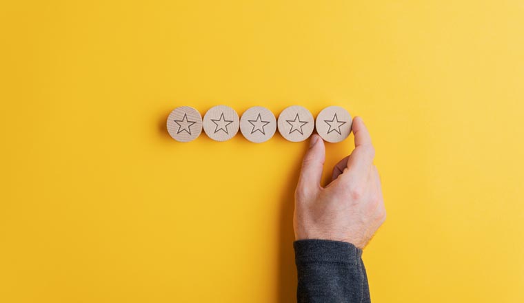 Male hand placing five wooden cut circles with stars on them in a row over bright yellow background. Conceptual image of quality and service.