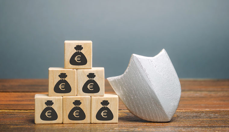 Wooden blocks with money and protection shield. Concept security of money, guaranteed deposits. Client rights protection. Compensation for losses in inflation, safeguarded investment capital.